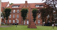 Historisches Gebäude aus roten Ziegeln mit Skulptur im Vordergrund.