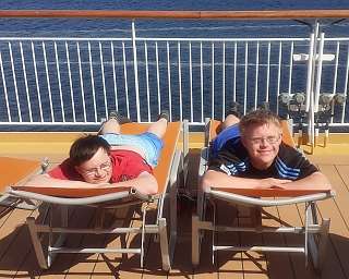Zwei Jungen entspannen auf Liegen an Deck eines Schiffes.