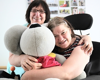 Zwei Frauen lächeln und umarmen ein großes Stofftier.