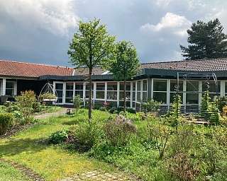 Blick auf einen gepflegten Garten mit einem Wohngebäude im Hintergrund.