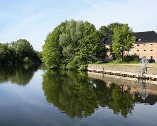 Spiegelung von Bäumen und einem Gebäude im Wasser.