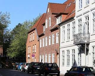 Blick auf eine Straße mit alten Häusern und parkenden Autos.
